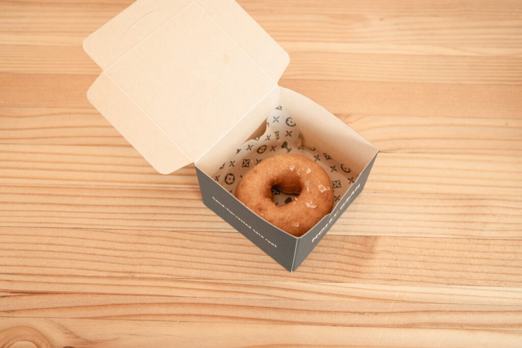 Holey Grail Donuts 的原味甜甜圈,放在印有品牌圖案的外帶盒中,擺在淺色木質桌面上。