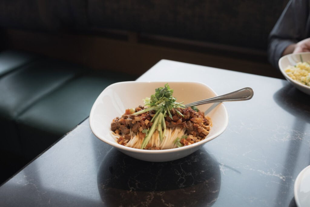 鼎泰豐川味牛肉拌醬麵，鋪上香菜、黃瓜絲與濃郁牛肉醬，裝在白色瓷碗中。