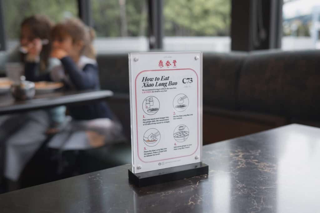 餐桌上立著一張小籠包吃法說明牌，兩位孩子坐在後方開心用餐。